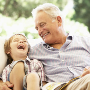 Grandfather With Grandson Reading Together On Sofa Laughing