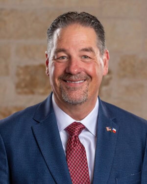 Peterson Health executive in a navy suit and red tie smiling in front of a beige brick wall.