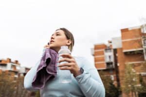 A woman drinking water outdoors after exercise, staying hydrated for health and wellness.