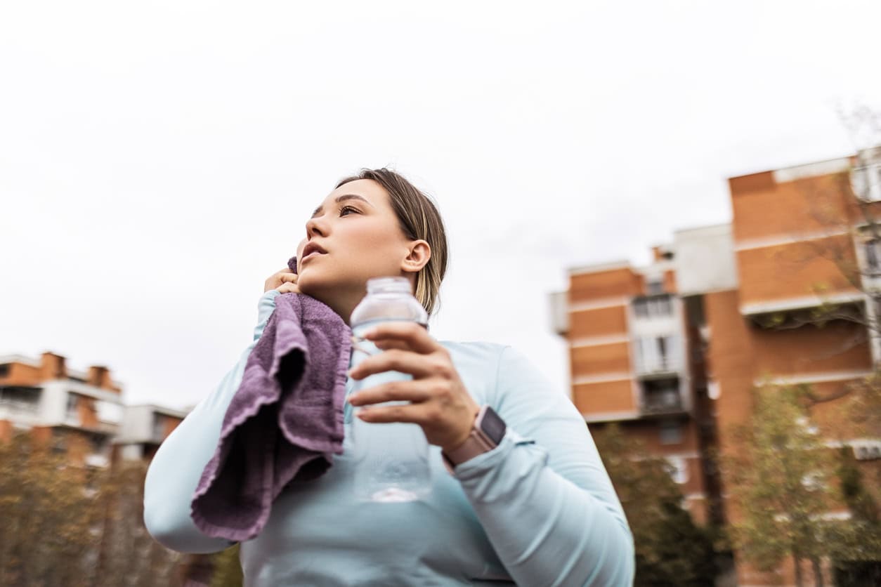 A woman drinking water outdoors after exercise, staying hydrated for health and wellness.