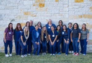 Group of healthcare professionals standing outdoors in front of a stone wall.
