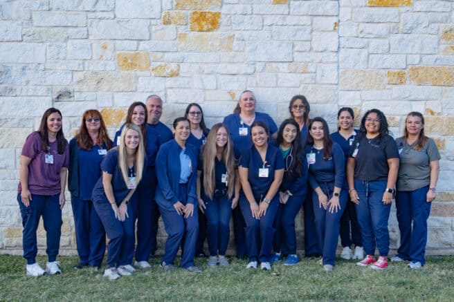 Group of healthcare professionals standing outdoors in front of a stone wall.