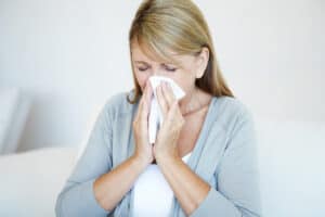 woman blowing runny nose in tissue during flu season