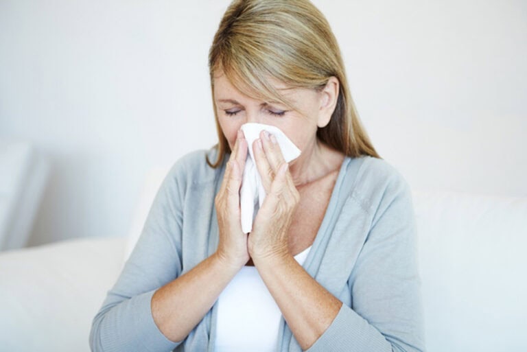 woman blowing runny nose in tissue during flu season