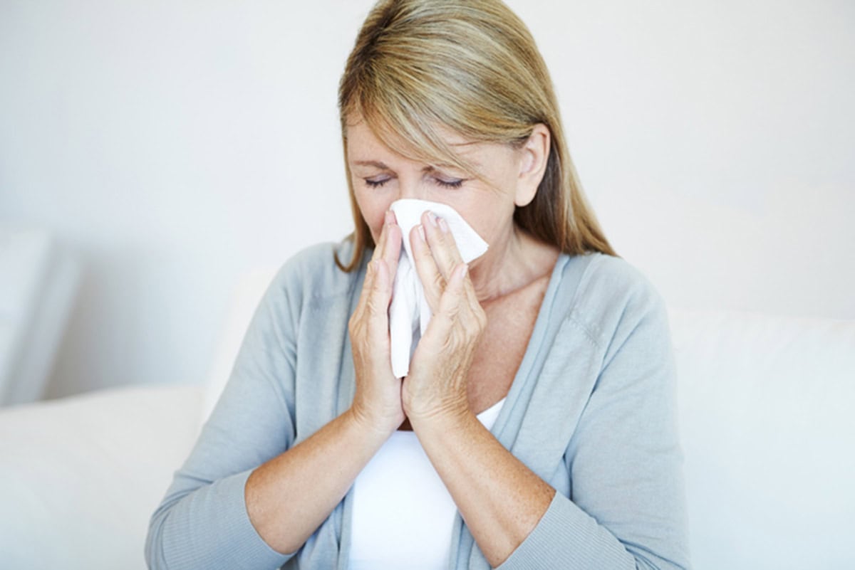 woman blowing runny nose in tissue during flu season